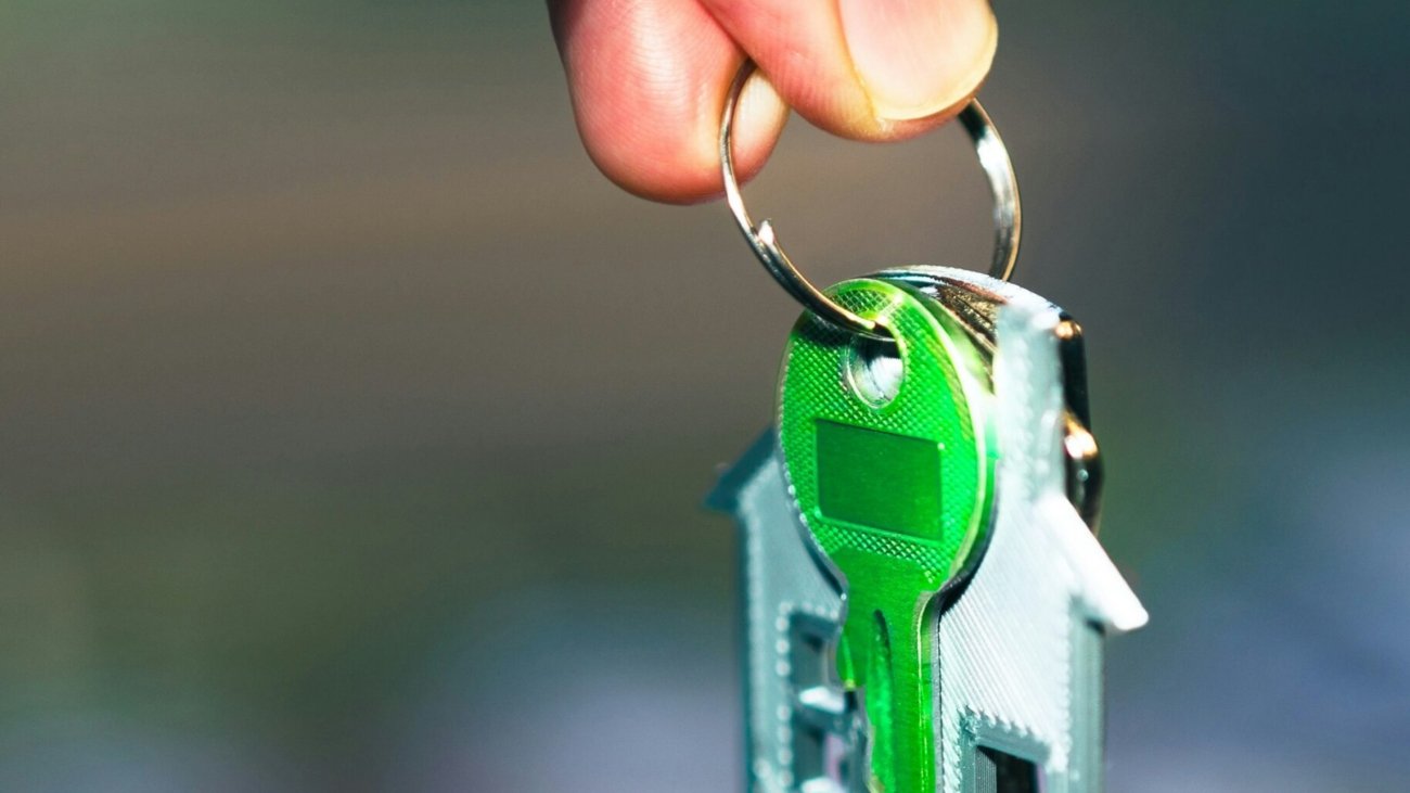 A hand holding a green key to a house